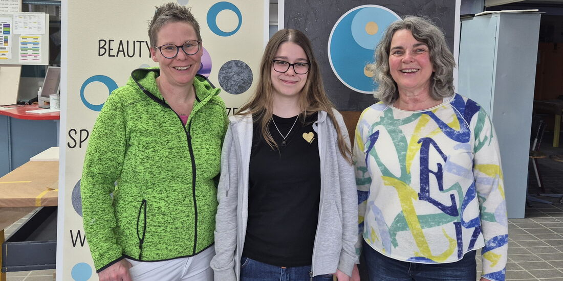 Emily Helmecke mit Ausbilderin und Sozialpädagogin vor den von ihr gestalteten Prüfungswänden.