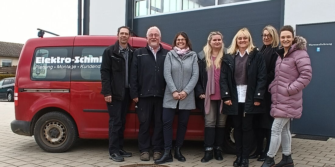 Die Geschäftsführung von Elektro-Schmitz zusammen mit der Abteilungsleitung des BFHs zusammen mit dem Team Plan B und einer Rehabilitandin vor einem roten Firmenwagen der Firma Elektro-Schmitz