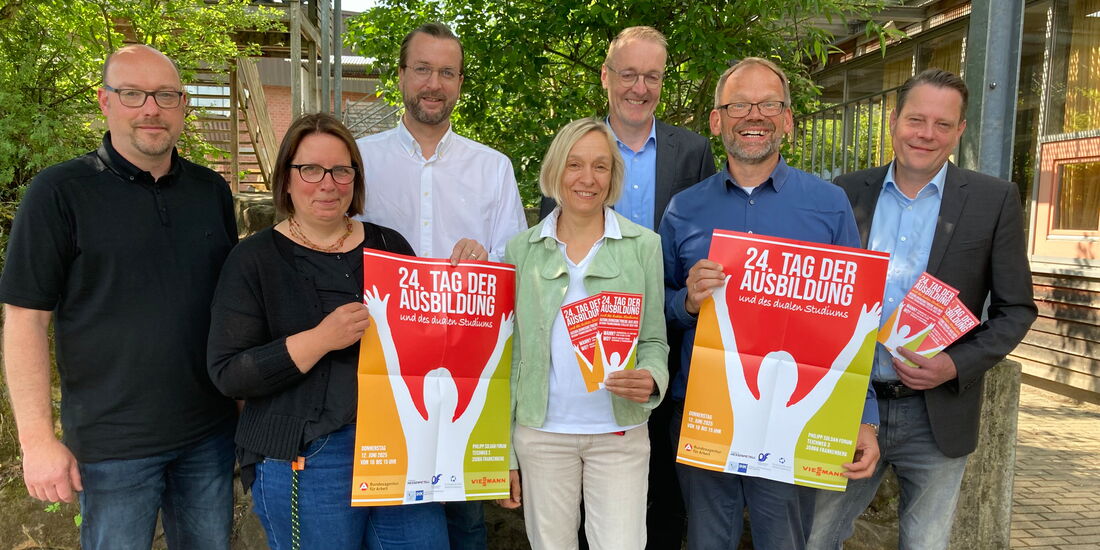 Sieben Veranstalter*innen mit Messeplakat und Flyern für den Tag der Ausbildung und des dualen Studiums vor der Ortenbergschule in Frankenberg.