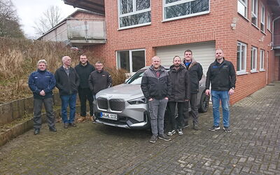 Auf dem Foto stehen die Teilnehmer der Hochvoltschulung gemeinsam mit ihrem Dozenten vor dem Gebäude des BFHI in Frankenberg. Der Dozent, Maximilian Werner, befindet sich auf der rechten Seite des Bildes. Einige Teilnehmer stehen vor einem Schulungs-PKW.