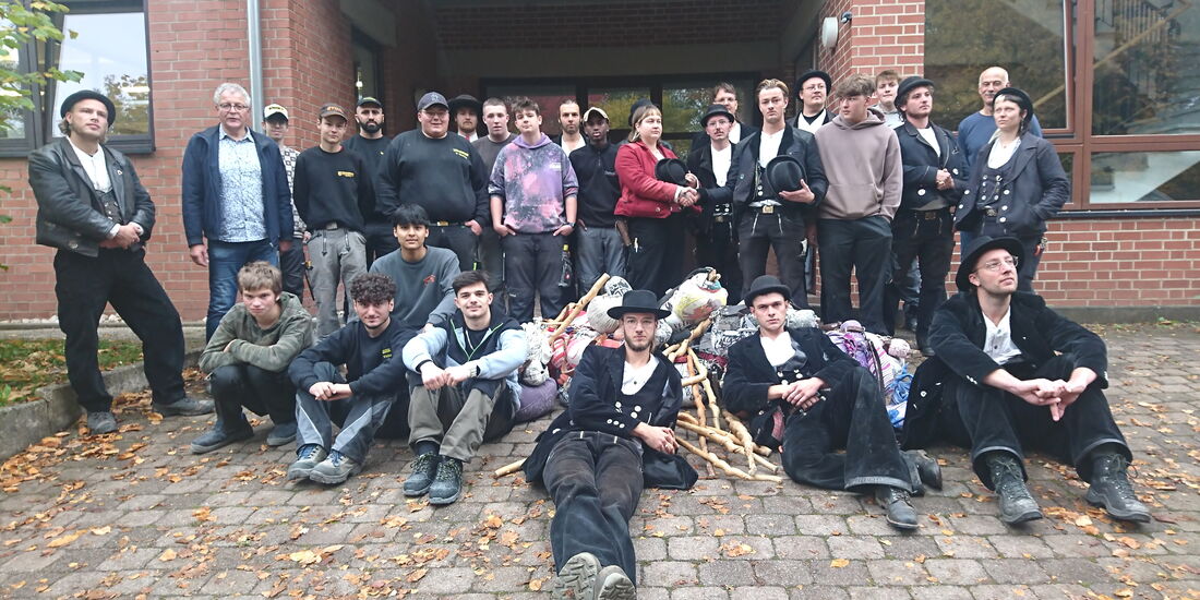 Gruppenfoto der Wandergesell*innen mit Ulrich Mütze, Peter Wilhelm und Auszubildenden vor dem Lehrbauhof Frankenberg.