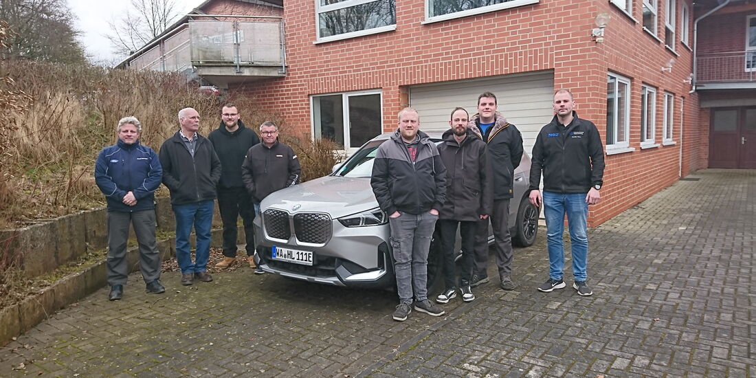 Auf dem Foto stehen die Teilnehmer der Hochvoltschulung gemeinsam mit ihrem Dozenten vor dem Gebäude des BFHI in Frankenberg. Der Dozent, Maximilian Werner, befindet sich auf der rechten Seite des Bildes. Einige Teilnehmer stehen vor einem Schulungs-PKW.